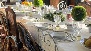 Une table à manger dressée pour un repas, avec des chaises, un élément décoratif au centre et une fenêtre avec des rideaux.