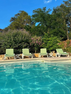 A pool area with four lounge chairs and a variety of trees and shrubs in the background.
