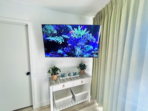 A television mounted on a white wall, with a wooden console below displaying the word "WELCOME".