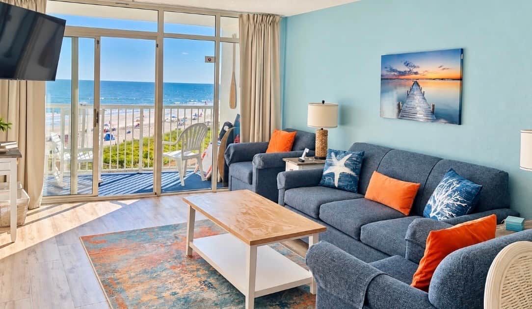 A living room with a sofa, coffee table, and a view of the beach through large windows.