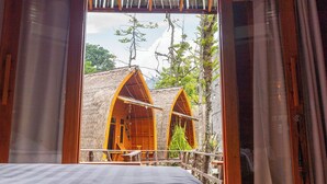 A room with a bed, wooden doors, and a view of two thatched-roof structures outside. - Torau Resort (Toinasa)