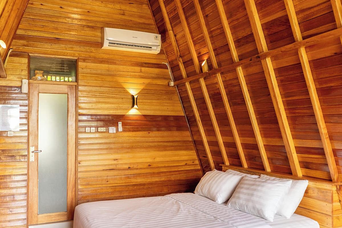 A cozy wooden cabin bedroom with a bed, a nightstand, a wall-mounted lamp, and an air conditioning unit.