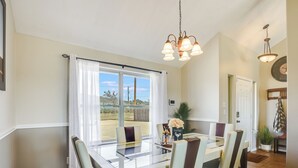 Un espace repas comprenant une table en verre, des chaises, un lustre et une vue sur l’extérieur.