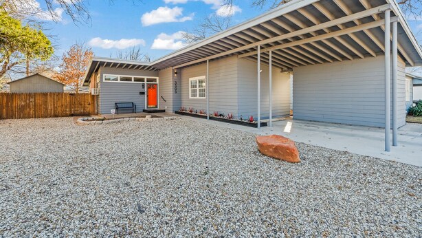 Una casa moderna con patio coperto, vialetto in ghiaia e recinzione in legno.
