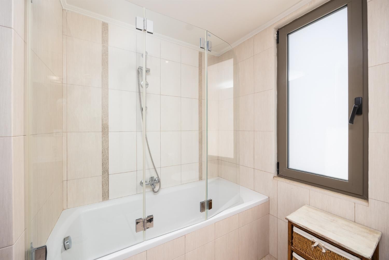 A modern bathroom with a glass-enclosed shower, a white bathtub, and a wooden vanity.