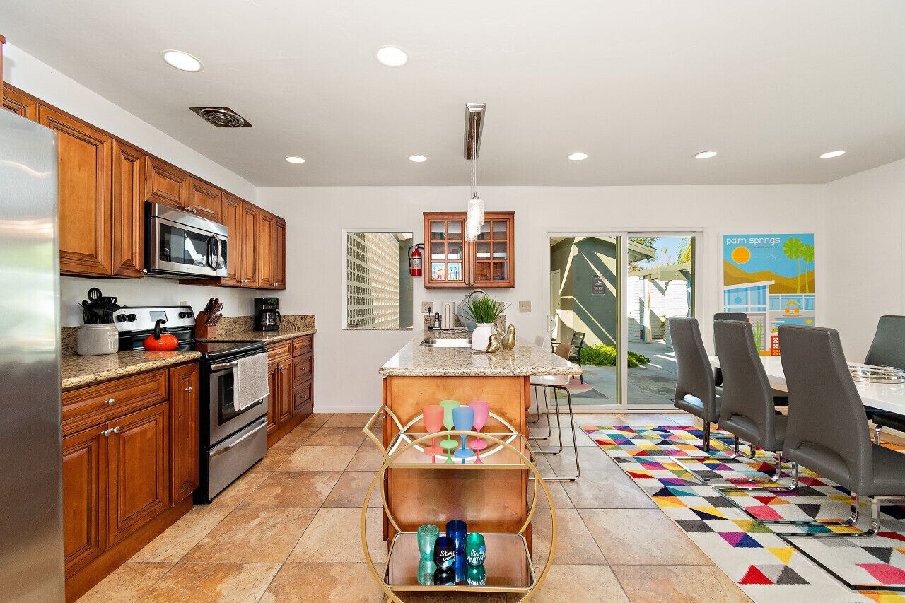 A modern kitchen with wooden cabinets, stainless steel appliances, and a central island with colorful glassware.