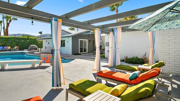 Un espace piscine avec des chaises longues et des parasols, un ciel dégagé et une vue sur un bâtiment en arrière-plan.
