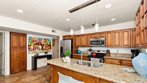 Une cuisine dotée de meubles en bois, de plans de travail en granit, d’appareils électroménagers en acier inoxydable et de luminaires suspendus.