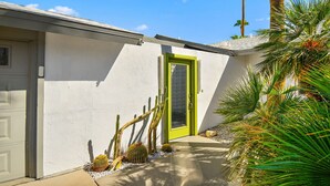 Un bâtiment à la façade blanche, avec une porte verte et un petit chemin menant à l’entrée.