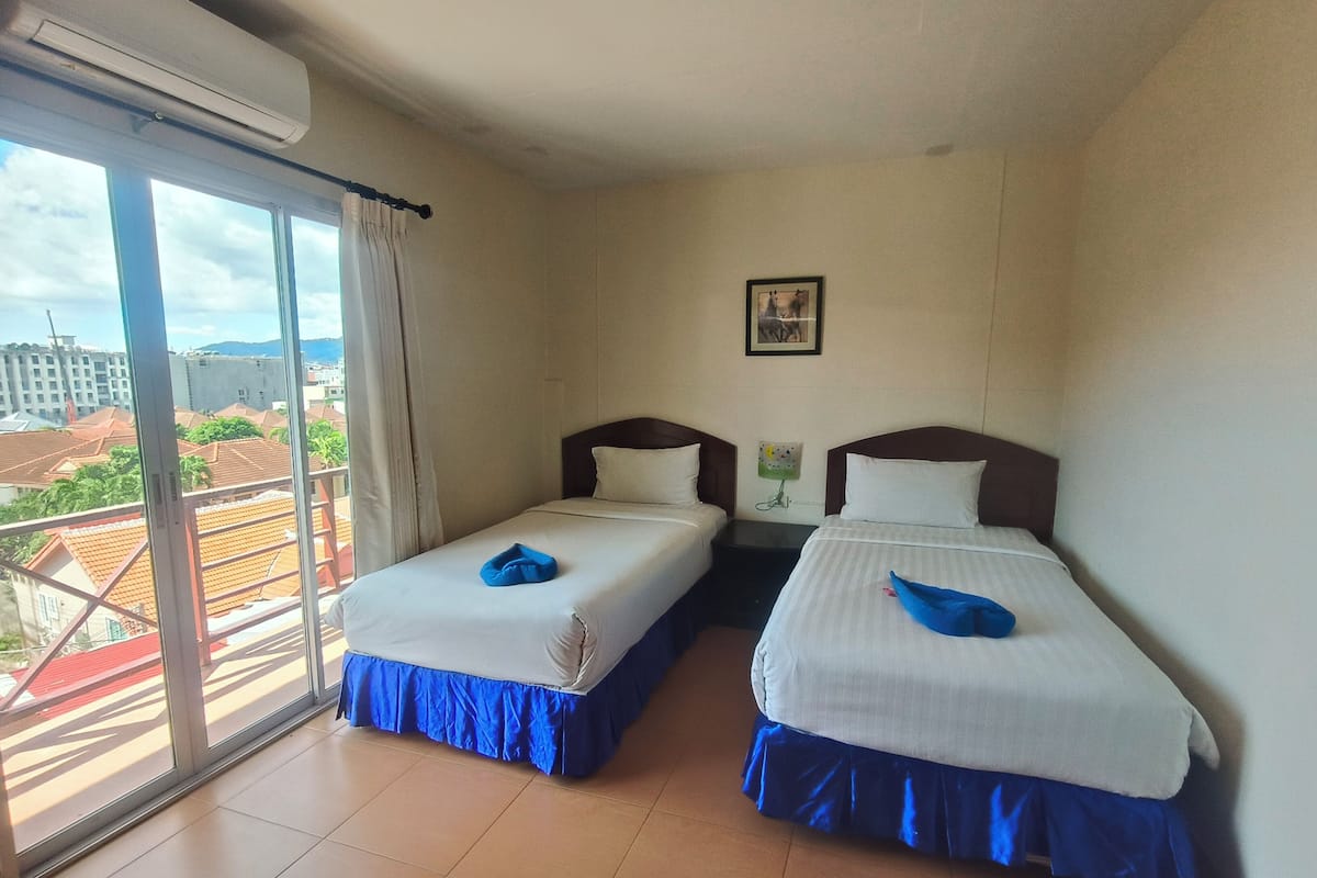 A hotel room with two beds, a large window, and a view of buildings outside.