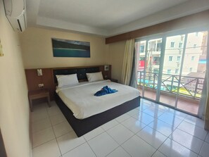 A hotel room with a bed, a painting on the wall, and a view of the outside balcony. - Bonanza Patong Hotel (Patong)