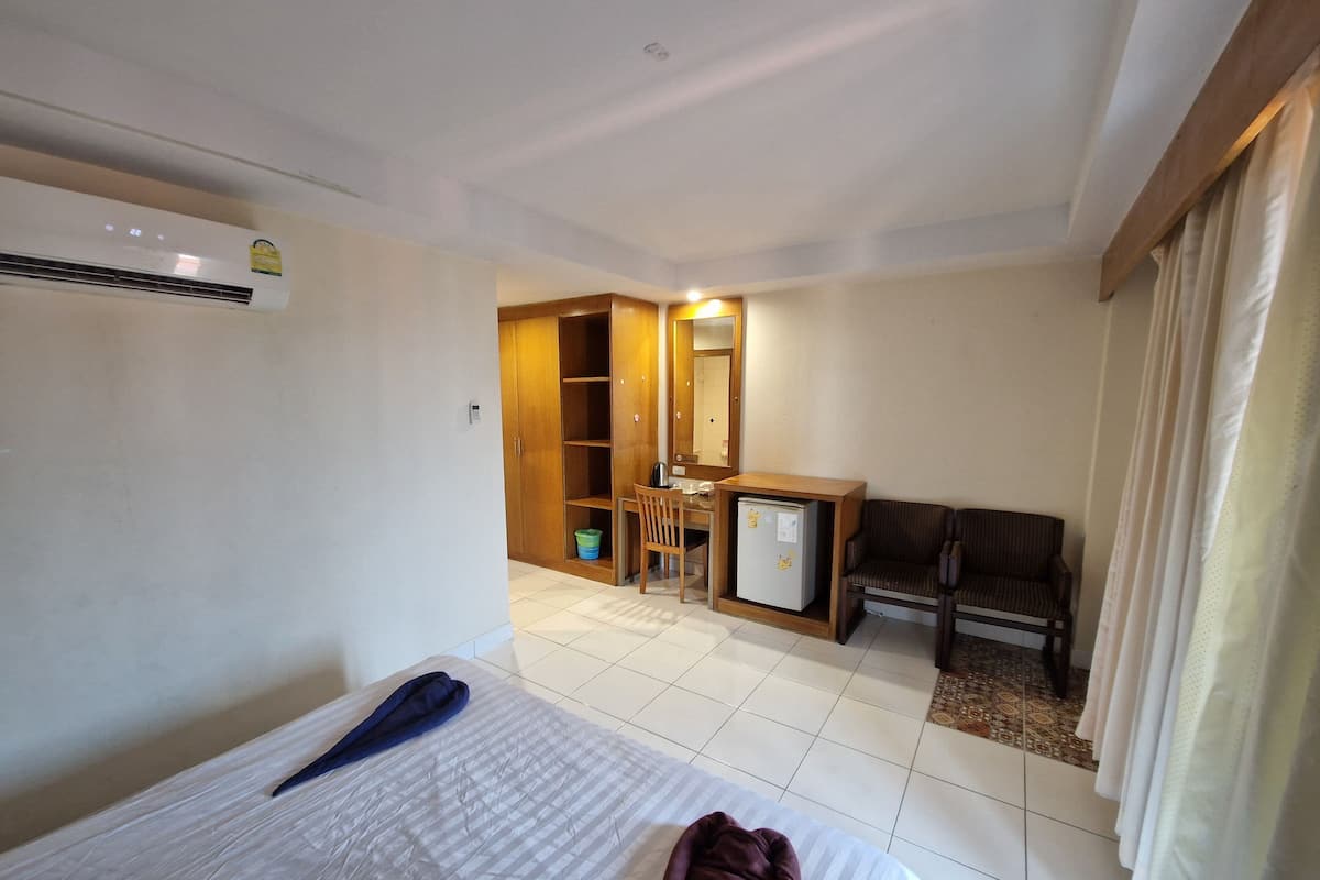 A hotel room with a bed, a desk, a chair, a small refrigerator, and a wardrobe.