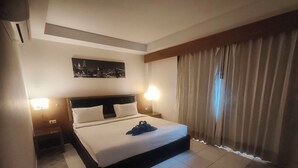 Hotelkamer met een groot bed, twee nachtkastjes, een schilderij van een stadsgezicht aan de muur, en een raam met gordijnen.