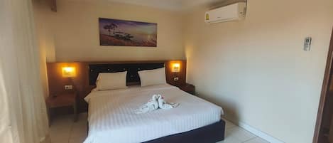 A hotel room with a large bed, two bedside lamps, a painting on the wall, and an air conditioning unit.
