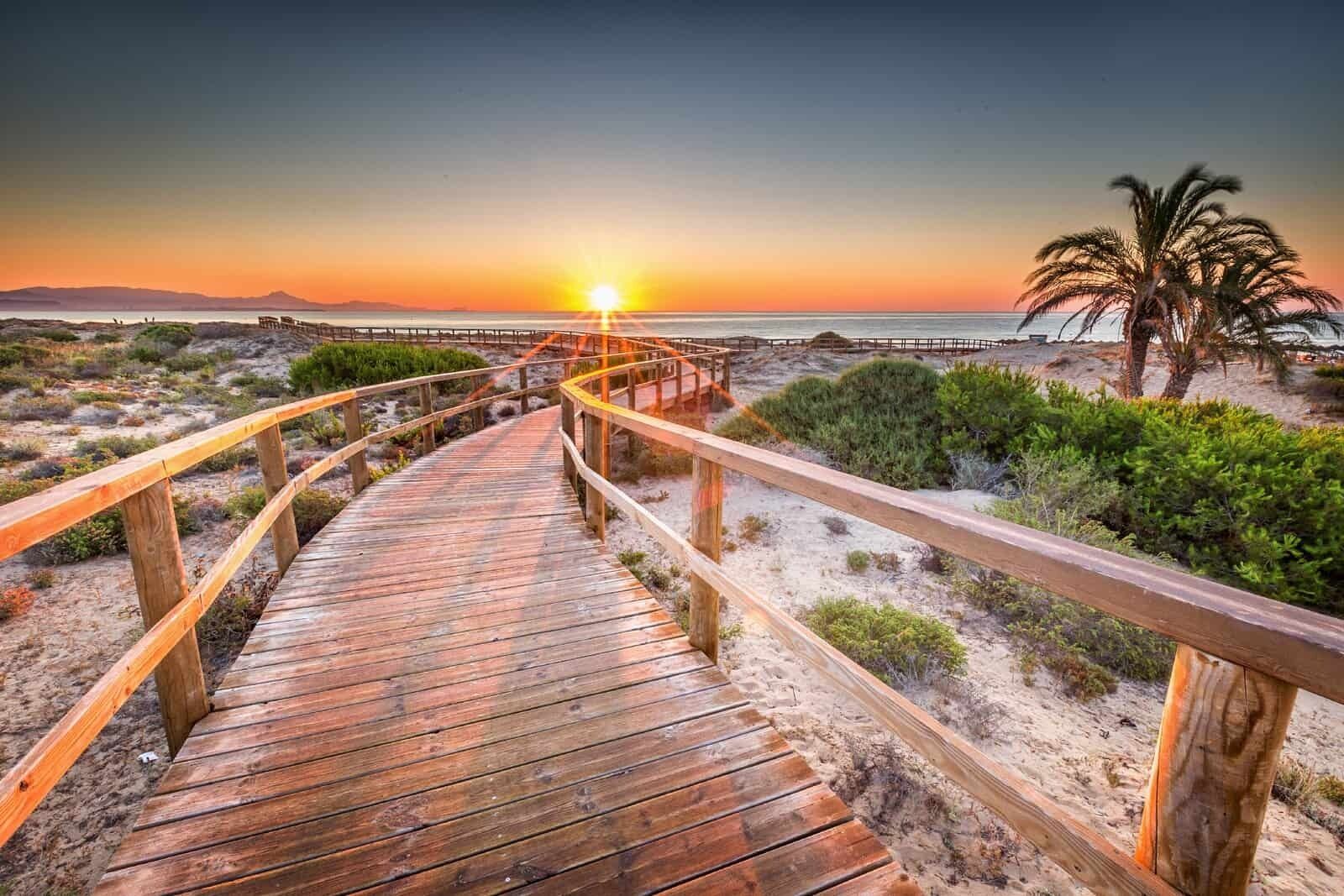 A wooden boardwalk leading to a beach with a sunset in the background.