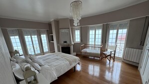 A spacious bedroom with a large bed, a crib, and a view of the sea through large windows. - Atlantic Views Sintra Guest House (Sintra)