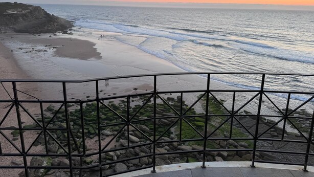 A coastal view from a balcony with a railing, overlooking a beach with waves and a sunset. - Atlantic Views Sintra Guest House (Sintra)