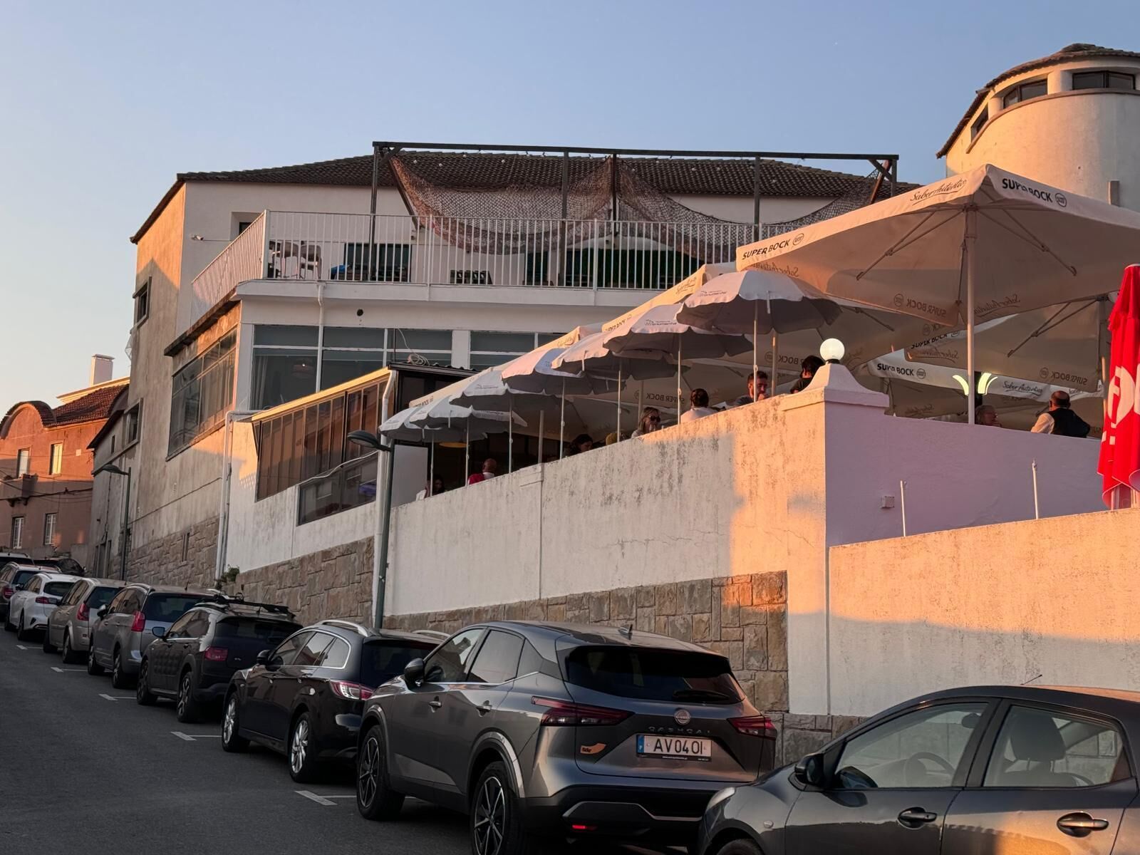 Une rangée de voitures garées devant un immeuble à la façade blanche, sur lequel flotte un drapeau rouge.