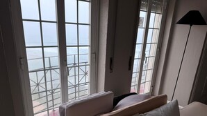 A hotel room with a large window overlooking a pier and the sea. There is a bed with white bedding and a floor lamp. - Atlantic Views Sintra Guest House (Sintra)