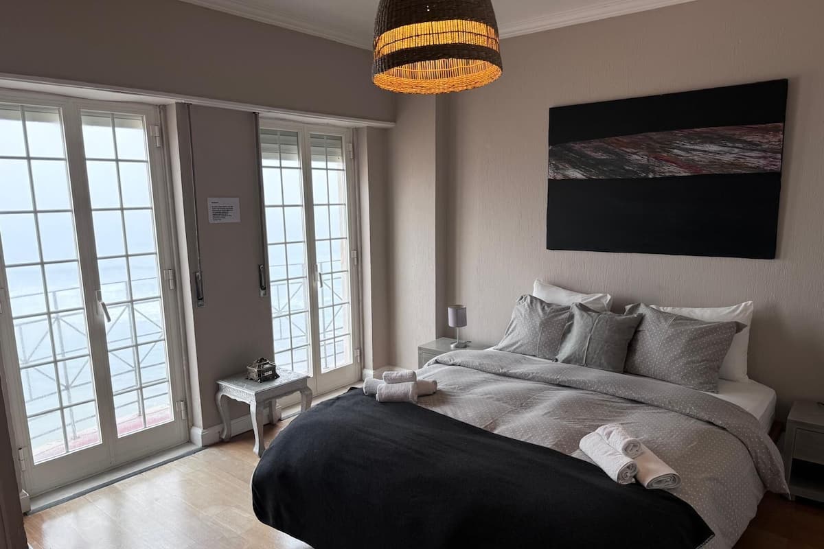 A bedroom with a large bed, a bedside table, a lamp, and a view through a sliding door.