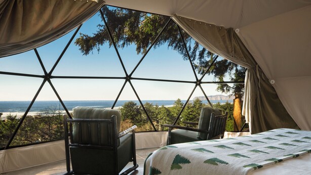 A tent with a bed and two chairs, a large window, and a view of the ocean. - Two Capes Lookout (Cloverdale)