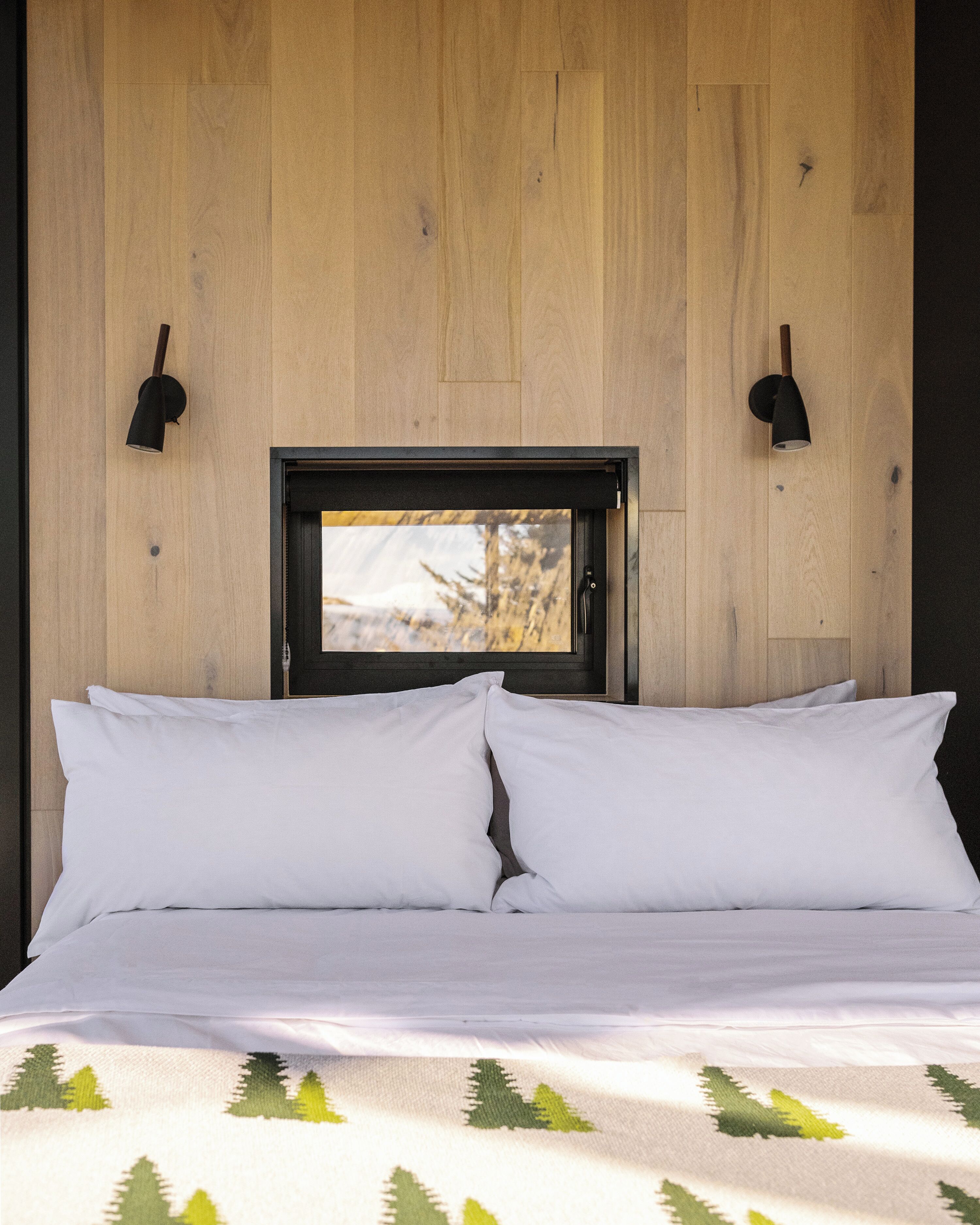 A bed with white linens and a view of trees through a window.