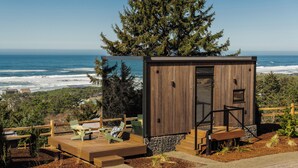 A wooden cabin with a door and a small porch area with seating. - Two Capes Lookout (Cloverdale)