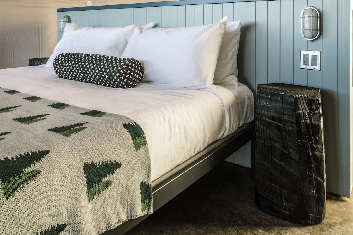 A bed with white and black patterned pillows, a beige blanket, and a green and white woven throw.