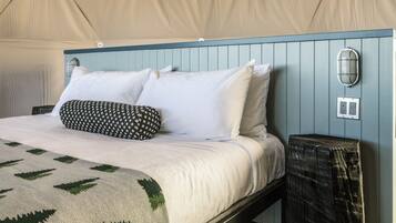 A bed with white and black patterned pillows, a beige blanket, and a green and white woven throw.