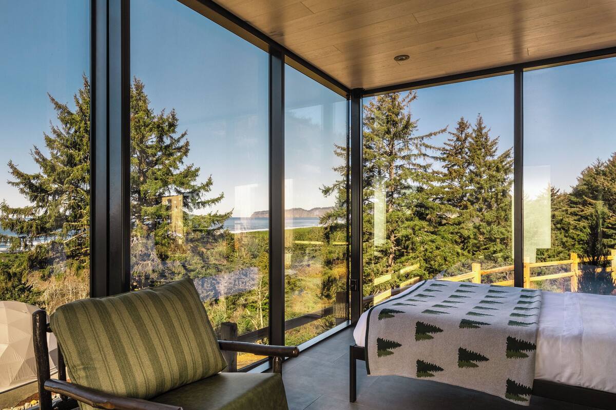A bedroom with a large window, a bed, a chair, and a view of trees and a cliff.