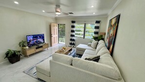 Una sala de estar con televisor, sofá y un amplio ventanal con cortinas.
