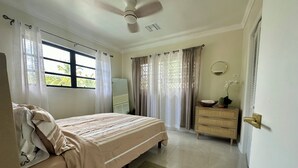 Un dormitorio con cama, cómoda, ventilador de techo y ventana con cortinas.