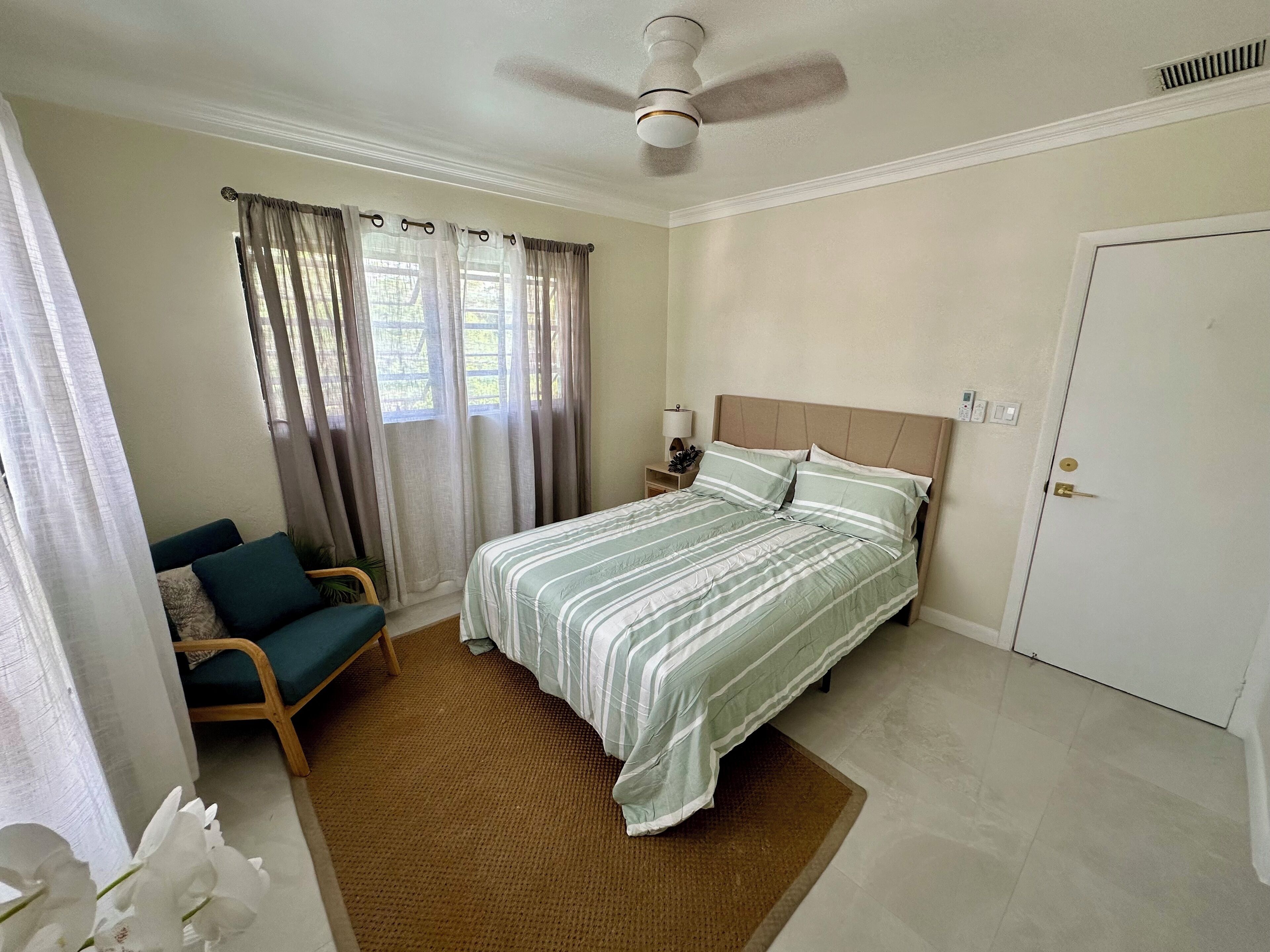 A bedroom with a bed, a chair, a nightstand, a ceiling fan, and a door.