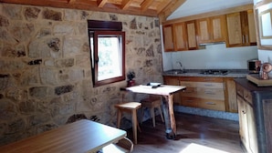 A rustic kitchen with stone walls, wooden cabinets, and a wooden table with stools. - House in Mar de Fóra (Fisterra) (Fisterra)