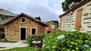 A stone building with a wooden door and windows, surrounded by lush greenery and flowers. - House in Mar de Fóra (Fisterra) (Fisterra)