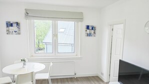 A bright, white room with a large window, a white table with chairs, a white cabinet, and a flat-screen TV. - Lovely flat near University of Aberdeen (Aberdeen)