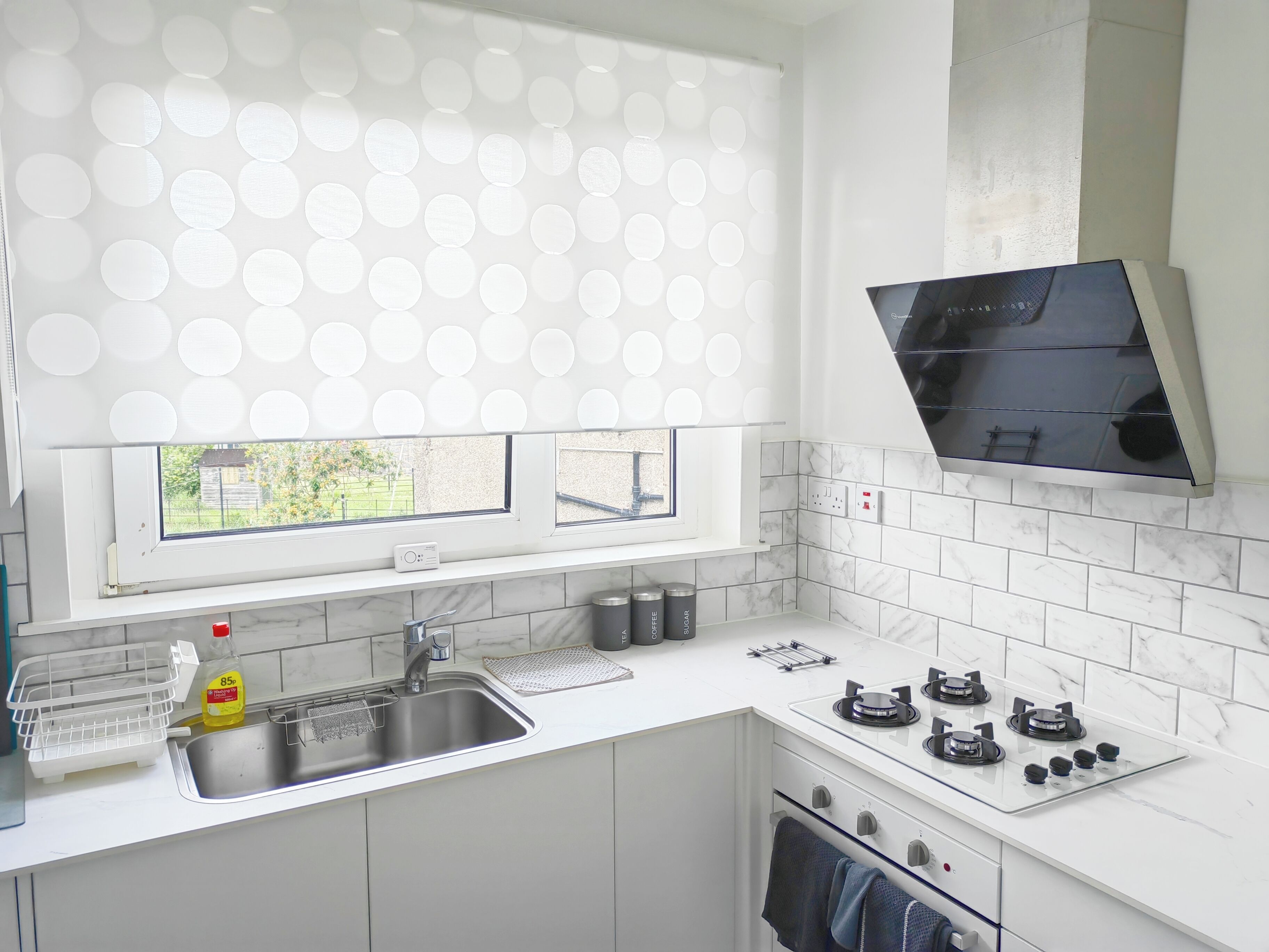 A modern kitchen with a window, white countertops, a sink, a stove, and a microwave.