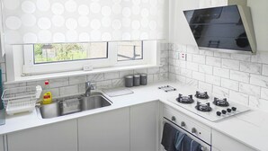 A modern kitchen with a window, white countertops, a sink, a stove, and a microwave. - Lovely flat near University of Aberdeen (Aberdeen)