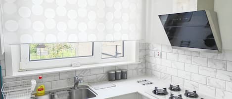 A modern kitchen with a window, white countertops, a sink, a stove, and a microwave.