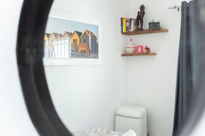 A room with a bed, a heater, a window with a view of houses, and shelves with books and a figurine.