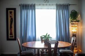 A dining area with a round wooden table, four chairs, a potted plant, and a wall-mounted light fixture.
