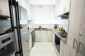 A compact kitchen with a built-in oven, microwave, and dishwasher, featuring light-colored cabinets and a granite countertop.