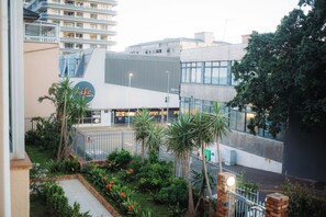 A modern building with a glass facade, surrounded by a landscaped garden with palm trees and flowering plants.