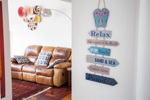 Una habitación con un sofá de cuero marrón, un cartel en la pared con flechas direccionales y una mesita con una lámpara.