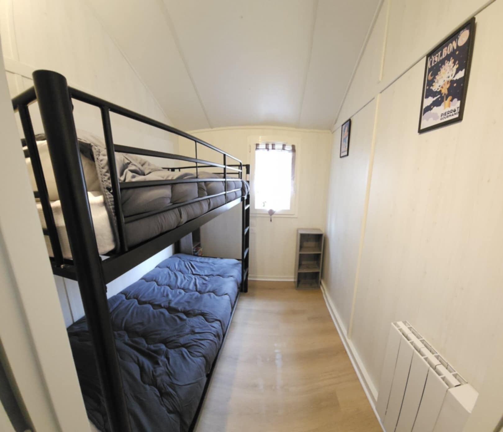 A narrow room with bunk beds, a window, a radiator, and a poster on the wall.