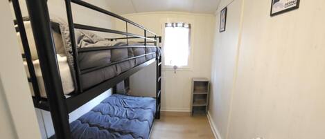 A narrow room with bunk beds, a window, a radiator, and a poster on the wall.