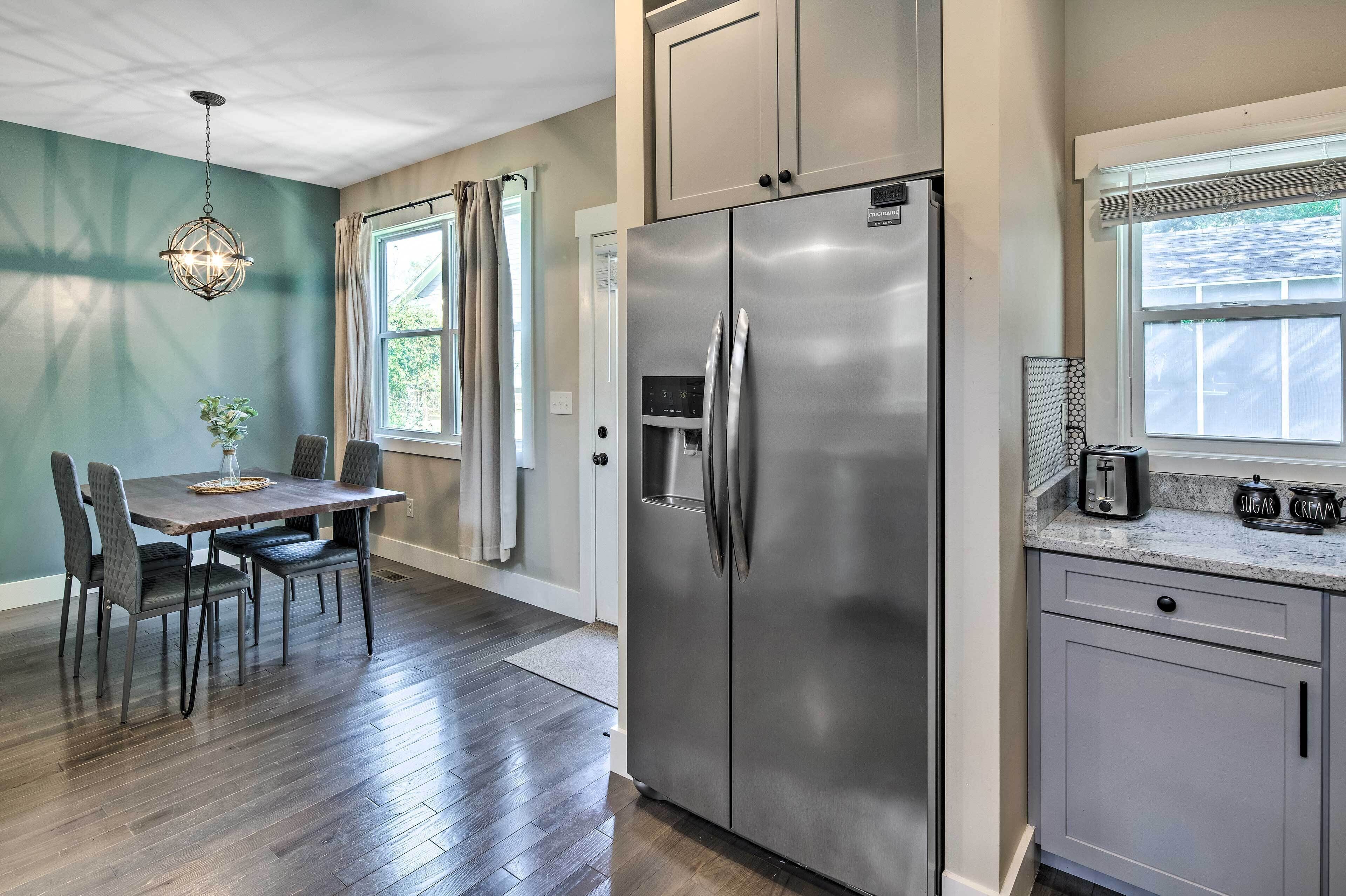A modern kitchen with a stainless steel refrigerator, a dining table with chairs, and a window with curtains.