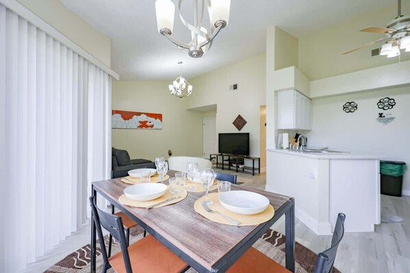 A dining area with a table set for four, a kitchen area, and a living room with a sofa and TV.
