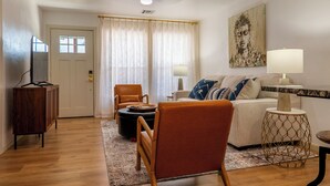 Una sala de estar con un sofá, dos sillones, una mesa de centro, una mesita con una lámpara, un aparador de madera y un ventilador de techo.