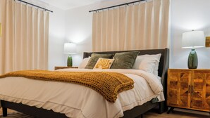 Un dormitorio con cama, cortinas, mesita de noche, lámpara y un armario de madera.